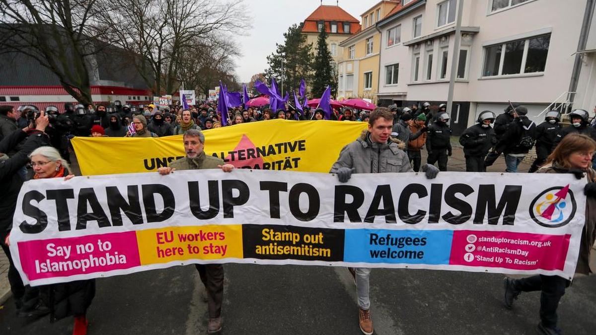 Manifestantes gritan consignas y sostienen una pancarta que dice “Enfrenta al racismo”, en camino al Centro de Congresos en Hannover, en el norte de Alemania.