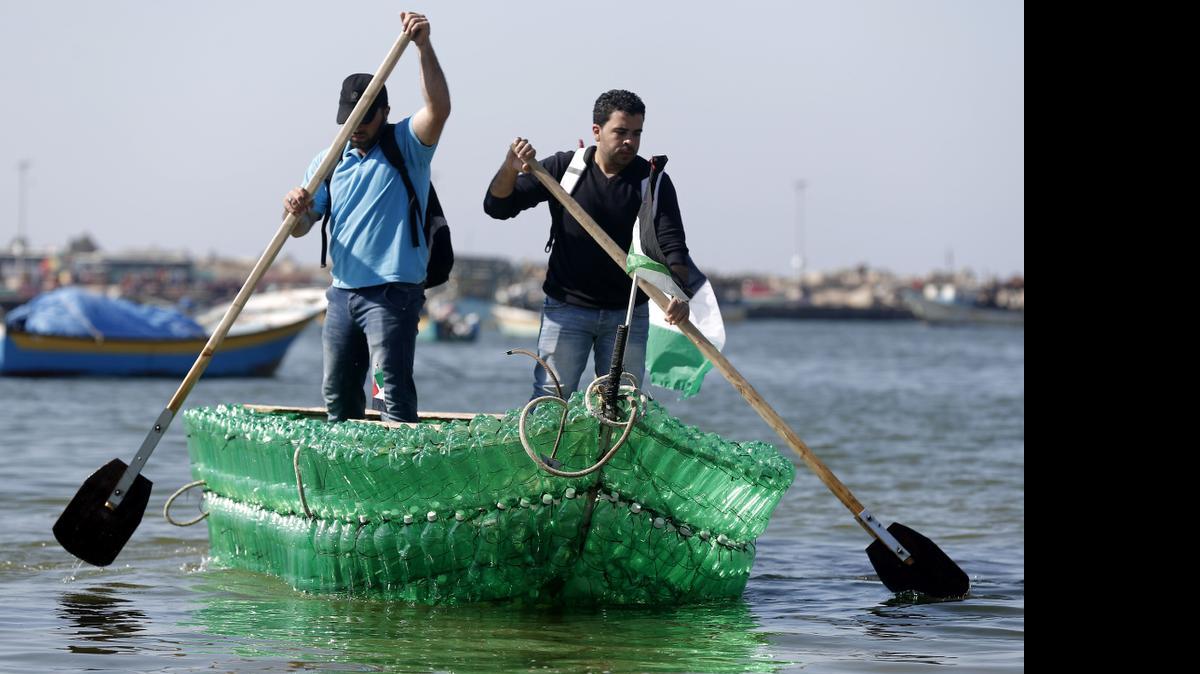 
Los palestinos Baha Abed (izq.) y su primo Mohamed Abed reman a bordo del bote que construyeron con botellas de plástico, en Gaza.
