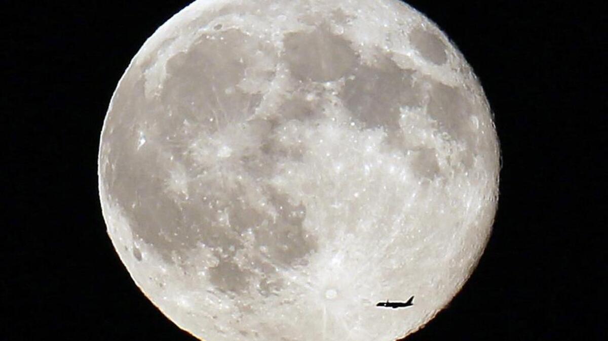 
Un avión comercial pasa en frente de la segunda luna llena del mes de julio, en Norfolk, Massachusetts.

