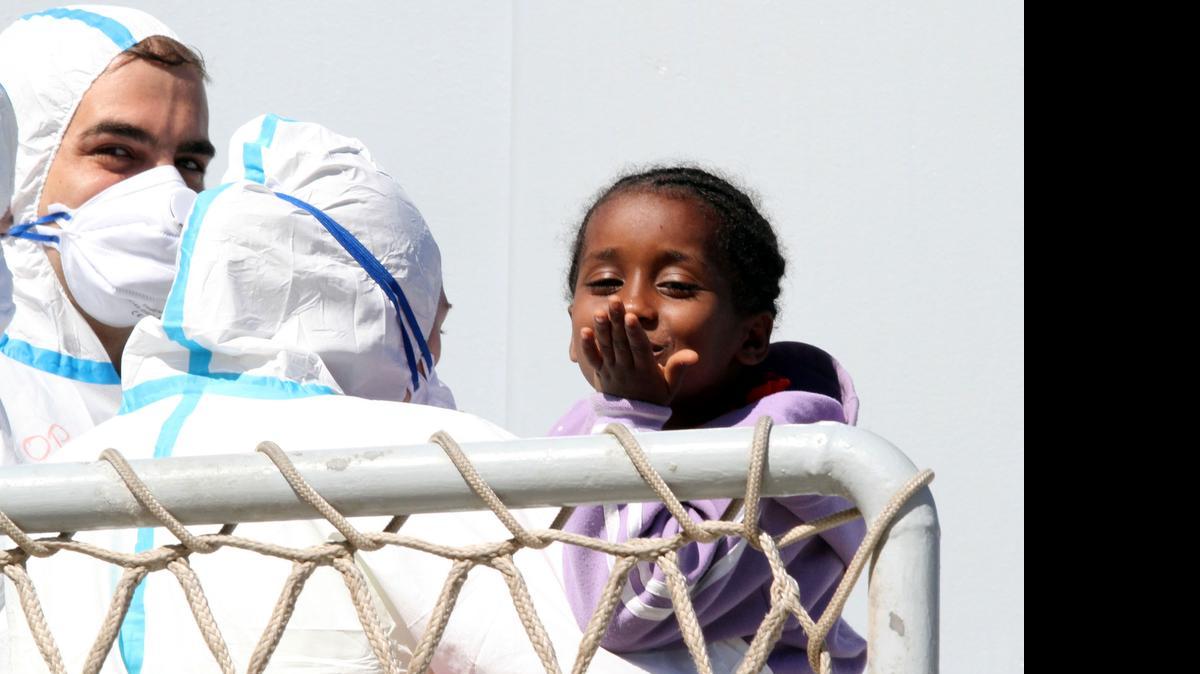 
Una niña migrante tira besos al ser rescatada en el mar por marineros de la Guardia Costera italiana.
