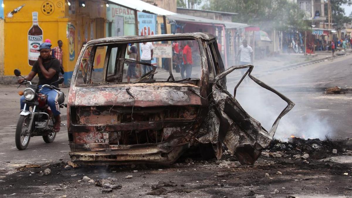 Un hombre pasa junto a los restos calcinados de un vehículo en Kinshasa, la capital de la Reública Democrática del Congo.
