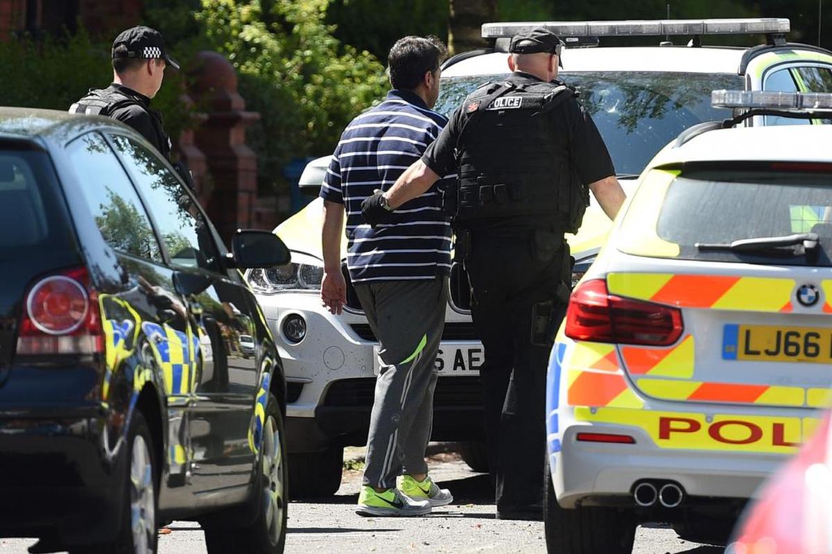 La policía escolta a un hombre de una propiedad en la avenida Dorset en Moss Side, Manchester, el 26 de mayo de 2017, tras una incursión en una propiedad residencial mientras sus investigaciones continúan en el ataque terrorista del 22 de mayo en el Manchester Arena.