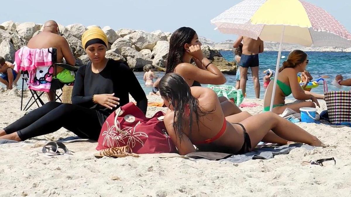 En una playa de Marsella, varias bañistas descansan, unas con bikinis y otra con un discreto burkini.