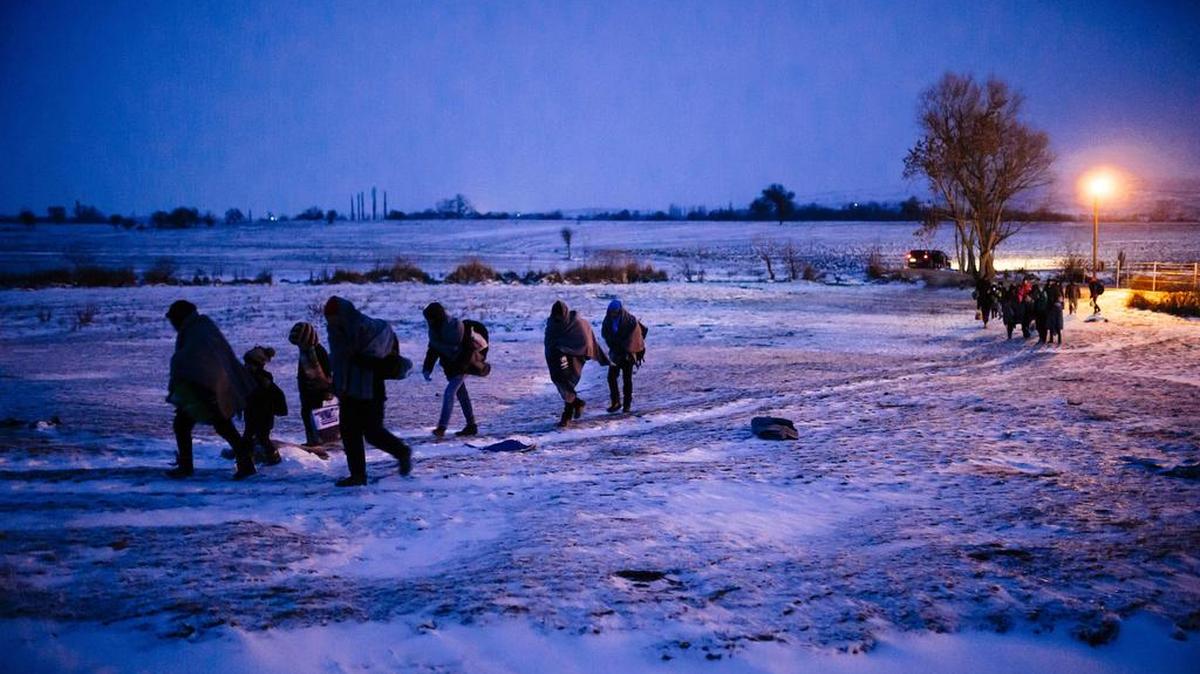 Migrantes y refugiados caminan por un campo cubierto de nieve tras cruzar la frontera de Macedonia con Serbia, cerca de la villa de Miratovac, este domingo.