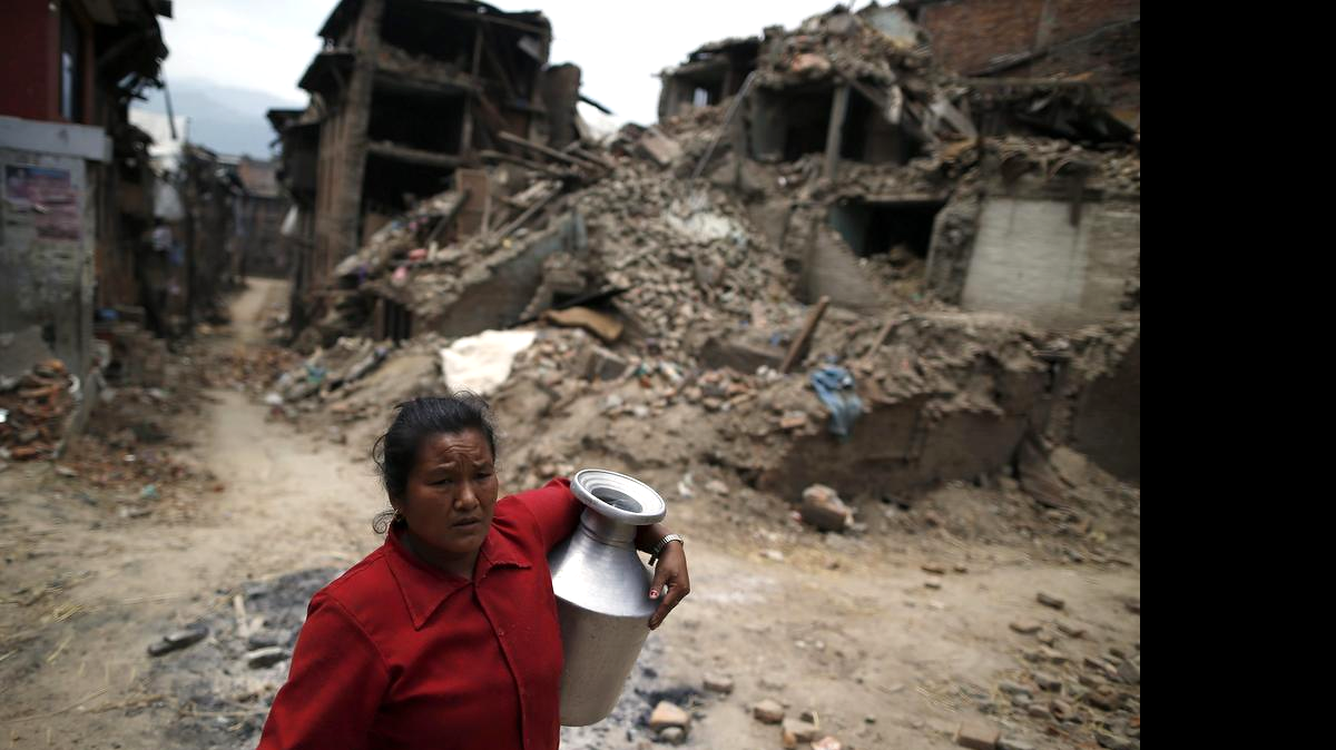 
 Una mujer carga con una garrafa de agua entre los escombros en Bhaktapur (Nepal), el viernes 15 de mayo de 2015. Detrás se puede ver cómo quedaron las calles luego del devastador terremoto. 