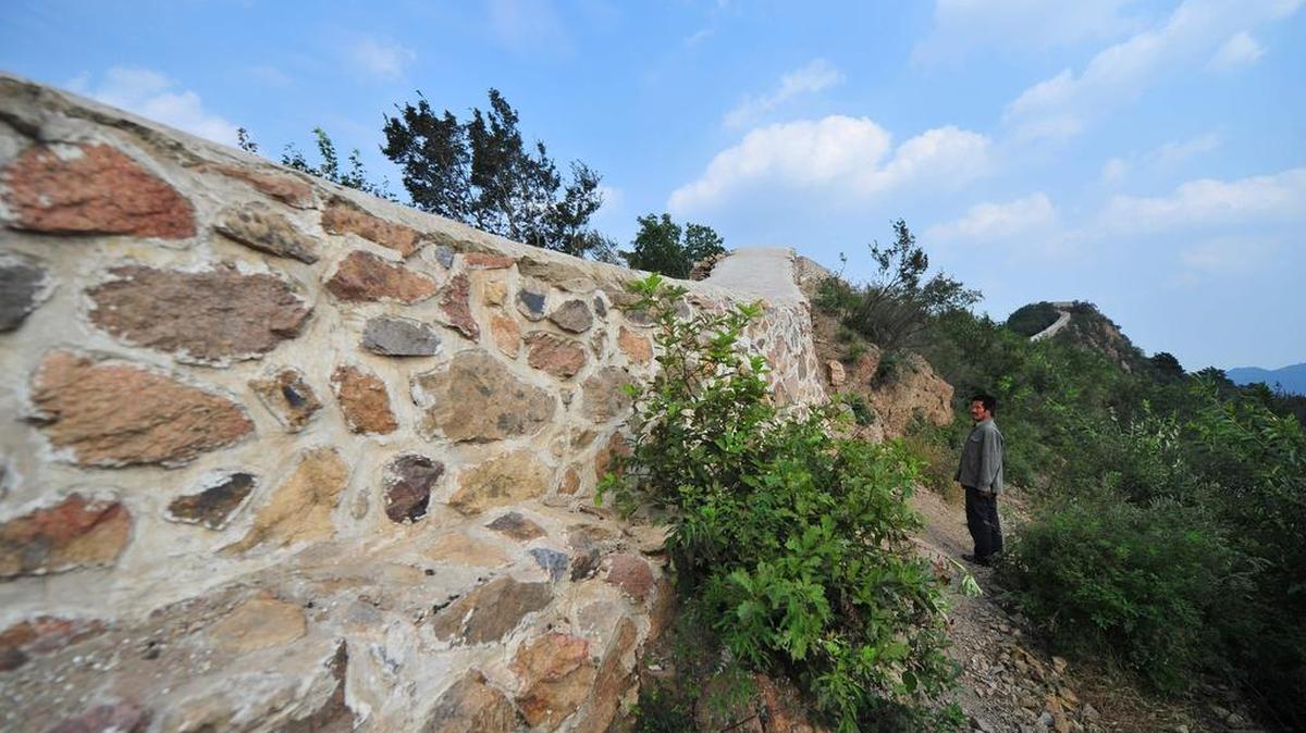Fotografía del 21 de septiembre de 2016 muestra un aldeano de pie junto a una sección reconstruida y pavimentada de la Gran Muralla de China en Suizhong, en el noreste de China.
