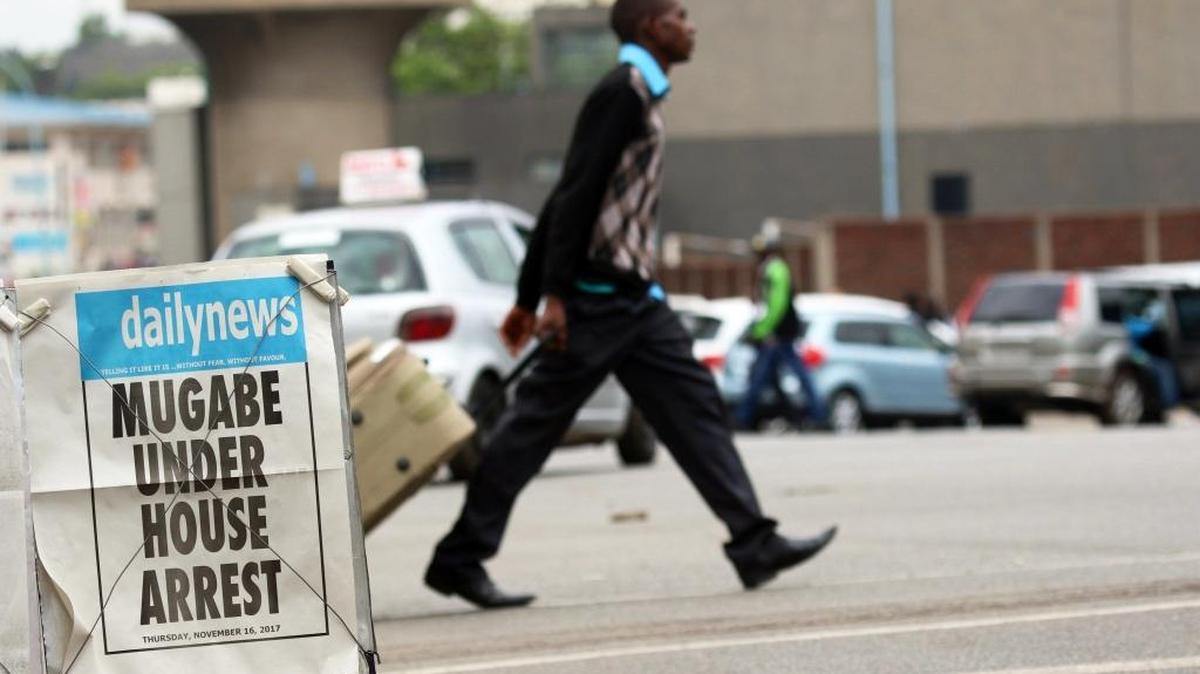 Una persona pasa junto a un cartel de un diario local que informa del arresto domiciliario del presidente Mugabe, en Harare, Zimbabue.