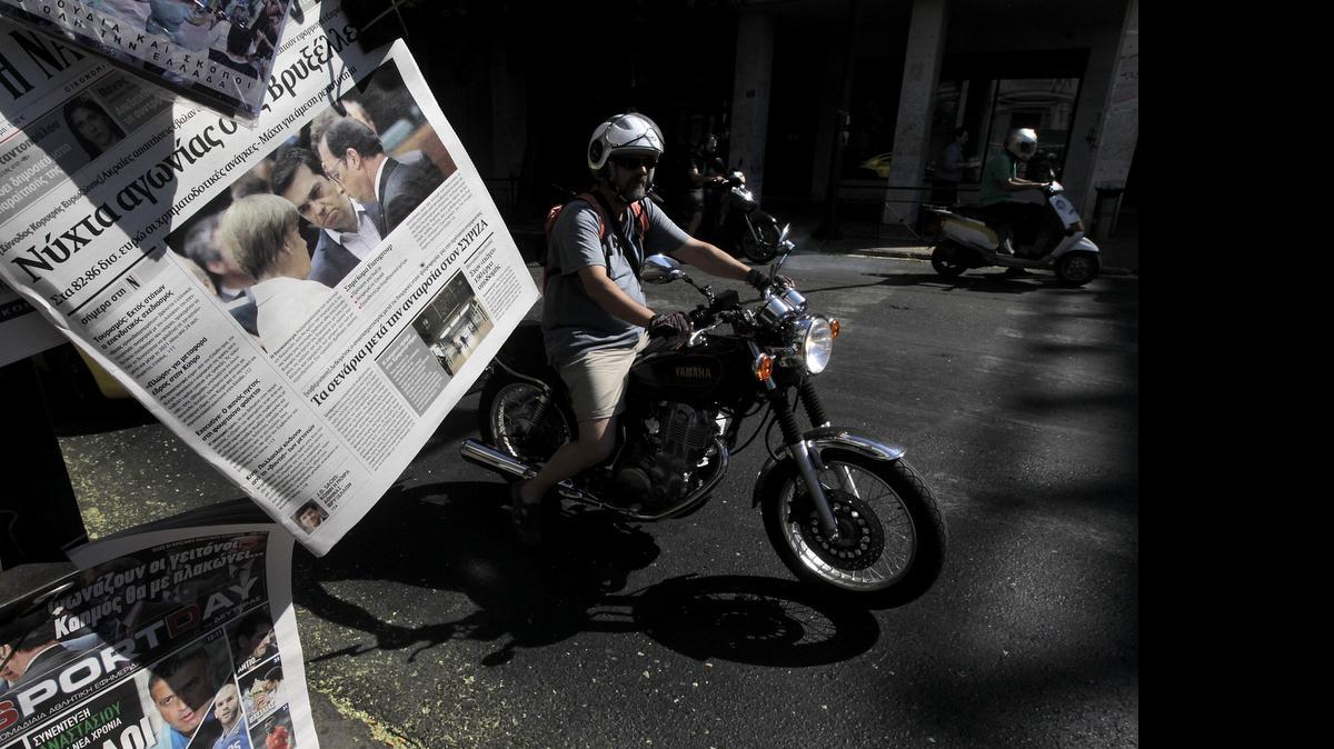 
Un motociclista pasa junto a un quiosco de periódicos en el centro de Atenas. La prensa local siguió muy de cerca el difícil acuerdo alcanzado para que Gracia no saliera de la eurozona.

