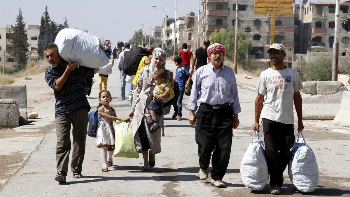 Familias sirias caminan con sus pertenencias al ser evacuados de la ciudad de Maadamiyet al Sham.