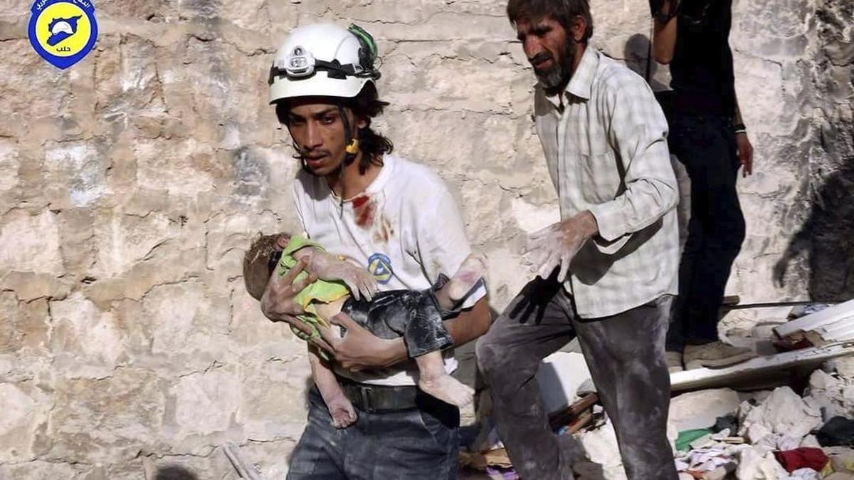 Fotografía sin fechar facilitada por la organización de voluntarios Defensa Civil Siria, el 7 de octubre de 2016, que muestra a dos voluntarios sirios mientras evacúan a un bebé tras un ataque en un lugar sin especificar en Siria.