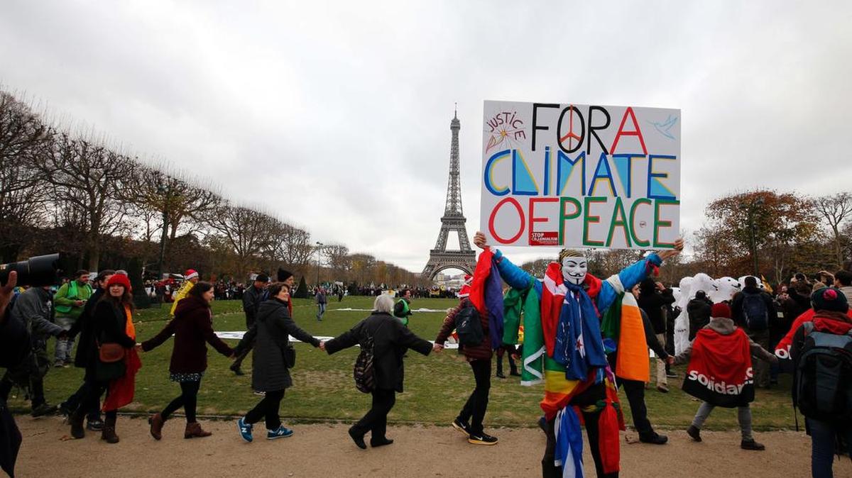 Un manifestante con una máscara del grupo Anonymous sostiene una pancarta que decía "Por un clima de paz" durante una manifestación convocada por varias organizaciones no gubernamentales (ONG) para formar una cadena humana en el Campo de Marte, cerca de la Torre Eiffel en París el 12 de diciembre 2015 sobre el marco de la COP21, la conferencia de la ONU sobre el calentamiento global.
