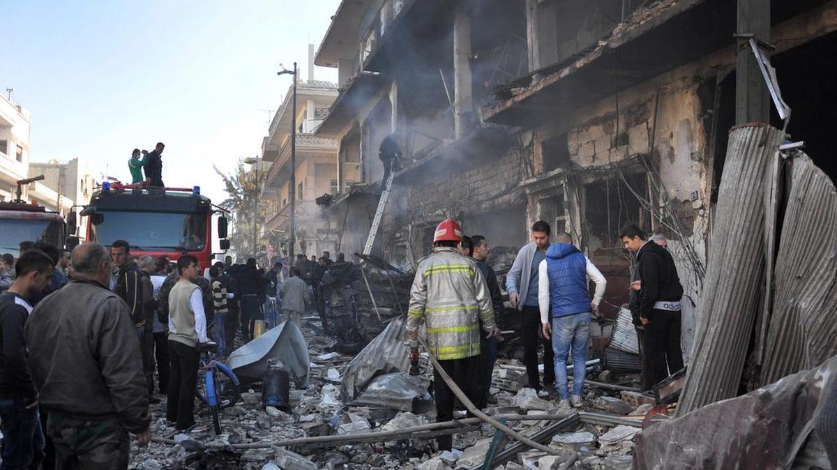 Ciudadanos y bomberos en el lugar de un atentado en Homs, Siria, este lunes, que ha dejado al menos 32 muertos y 90 heridos.