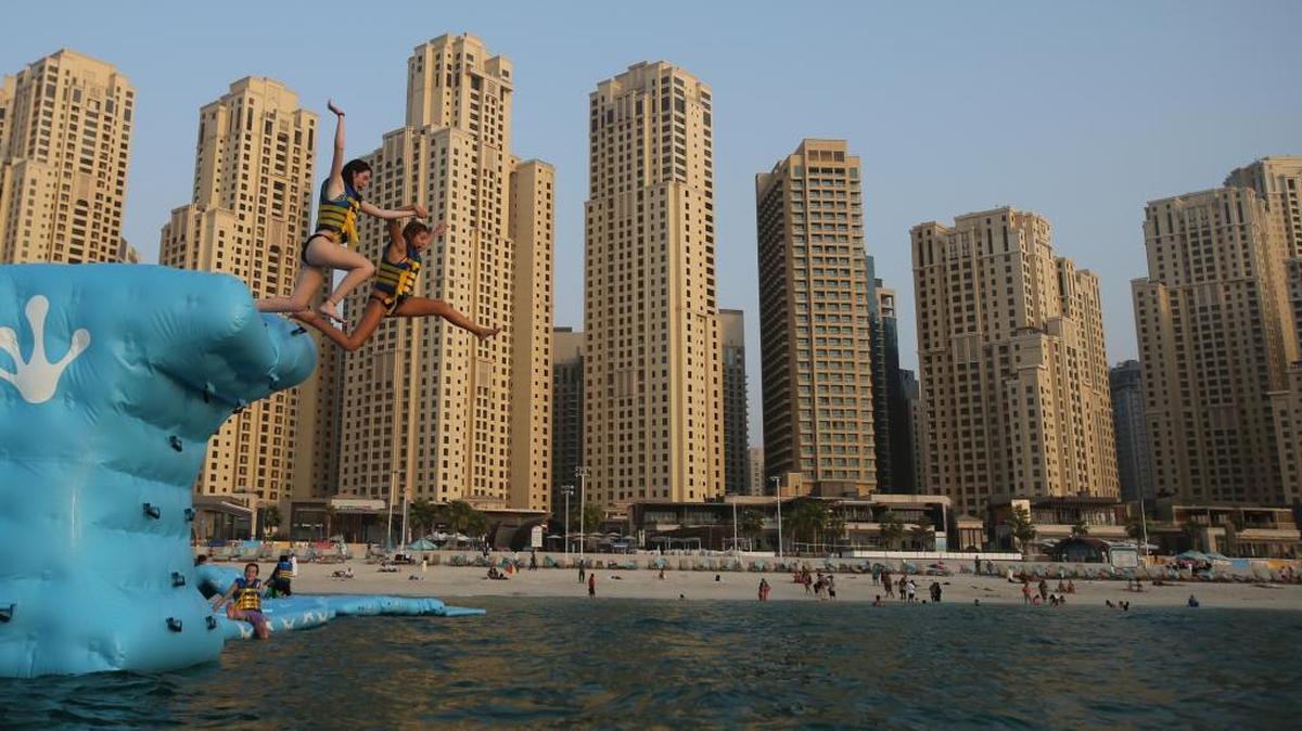 Dos mujeres saltan en un parque de agua frente Jumeirah Beach Towers en Dubái. ,