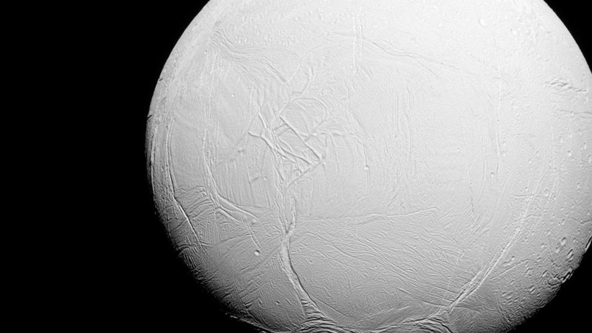 Esta foto de 27 de julio 2015 hecha por la nave espacial Cassini muestra la luna Enceladus orbitando el planeta Saturno. Hacia el norte, la parte superior, el terreno está cubierto de cráteres de impacto, al igual que otras lunas heladas, pero hacia el sur, el registro de cráteres de impacto es mucho más escasa, y en lugar de la tierra está cubierta de fracturas y largas, características lineales.