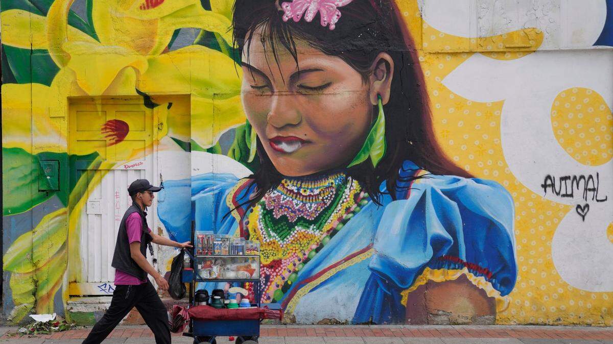Un vendedor de flores camina frente a un mural de una mujer indígena, en Bogotá, Colombia, el viernes 11 de noviembre de 2022. (Foto AP/Fernando Vergara)