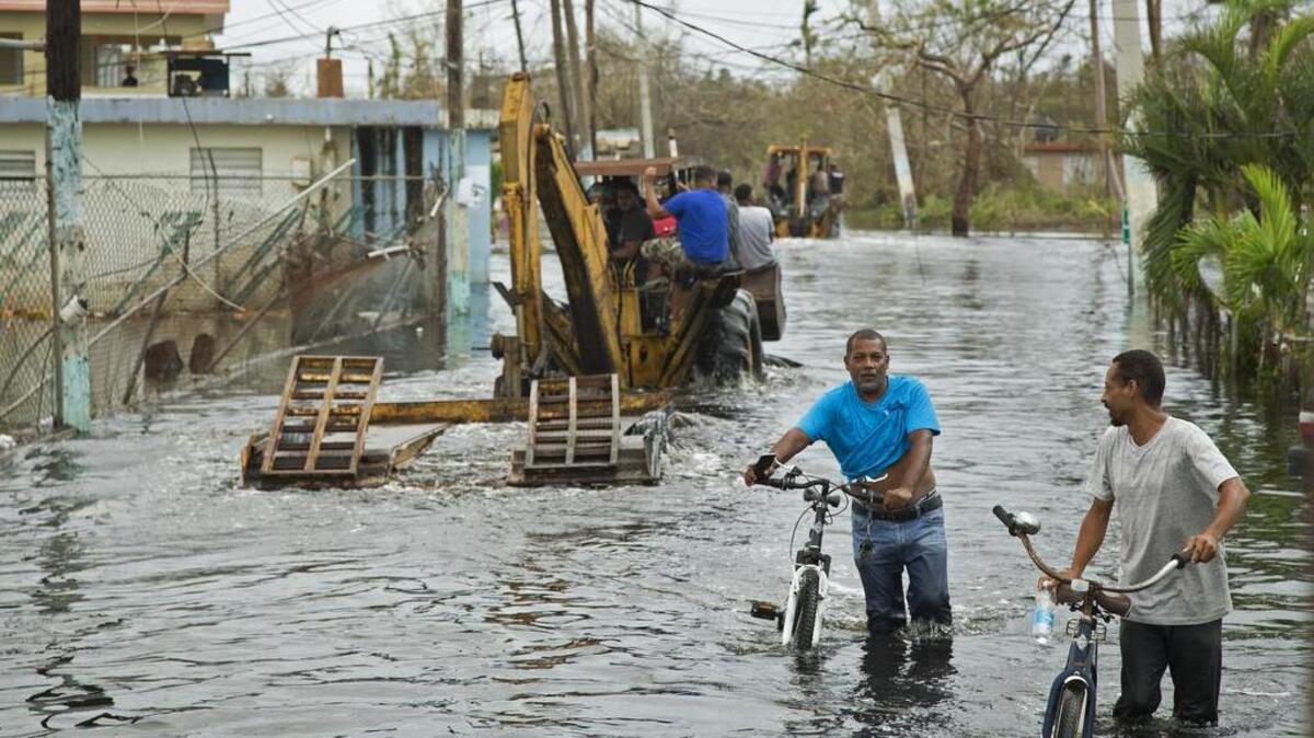 Residentes del pueblo de Loíza en Puerto Rico en la comunidad de Miñi Miñi usan maquinaria pesada para ayudar a sus vecinos en áreas inundadas después del huracán María, y otros caminan en las aguas inundadas con sus bicicletas. En toda la isla de Puerto Rico solamente había poco más de 1,000 pólizas de seguro contra inundaciones cuando tocó tierra el huracán María en una isla de más de 3.5 millones de habitantes.