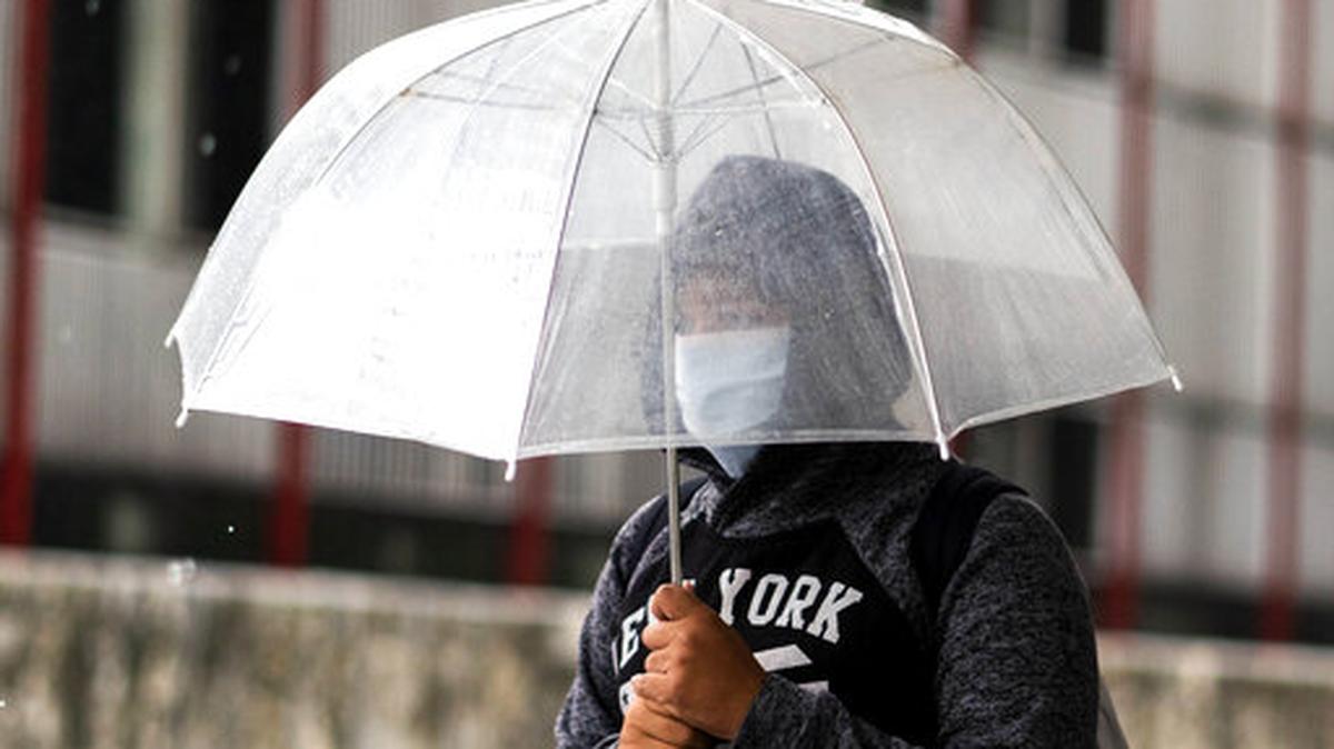 Una persona usa una máscara como precaución contra la propagación del nuevo coronavirus bajo una sombrilla mientras llueve en Montevideo, Uruguay, el miércoles 18 de marzo de 2020.