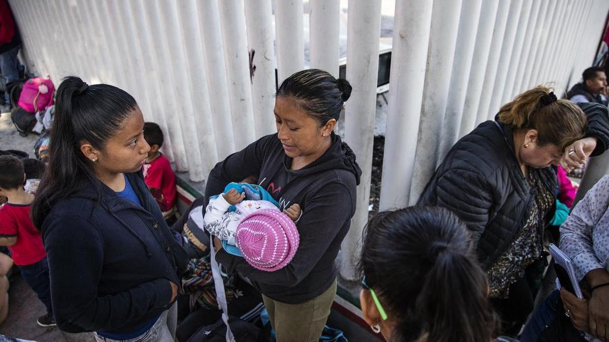 Una mujer de Guatemala, con sus hijas, espera en junto a la valla fronteriza en Tijuana para entrar en Estados Unidos y pedir asilo, el 14 de junio.