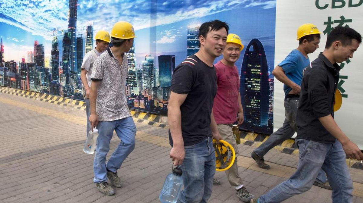 Obreros de la construcción pasan junto a un mural del Distrito Comercial Central de Pekín, el 10 de julio.