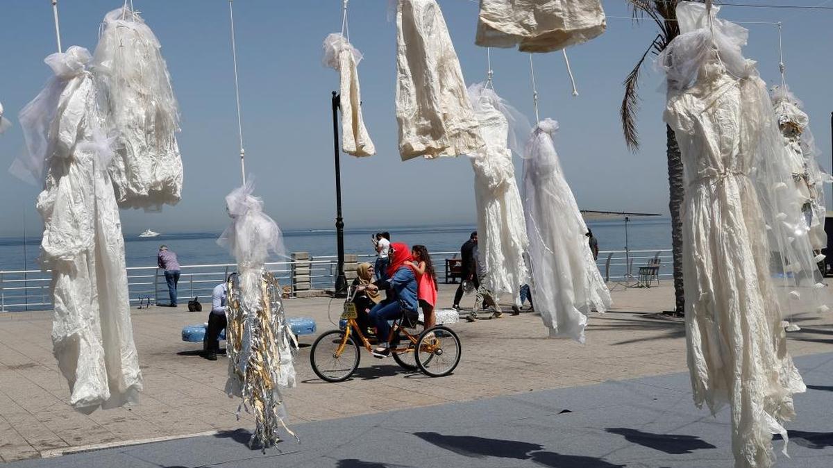 Una mujer y su hija pasan en bicicleta junto a vestidos de novia colocados por una ONG en la costa del Líbano en Beirut, en abril, en protesta por una antigua ley que perdona a un violador si se casa con la víctima. La ley fue derogada el pasado agosto.