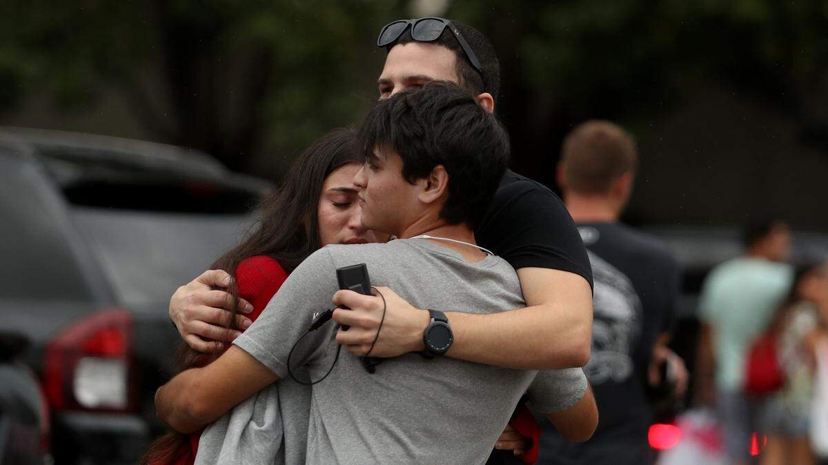 Tres personas se abrazan frente al centro comercial Town Center en Boca Raton, el domingo 13 de octubre de 2019, en donde se reportó la presencia de un atacante armado. El reporte fue una falsa alarma.