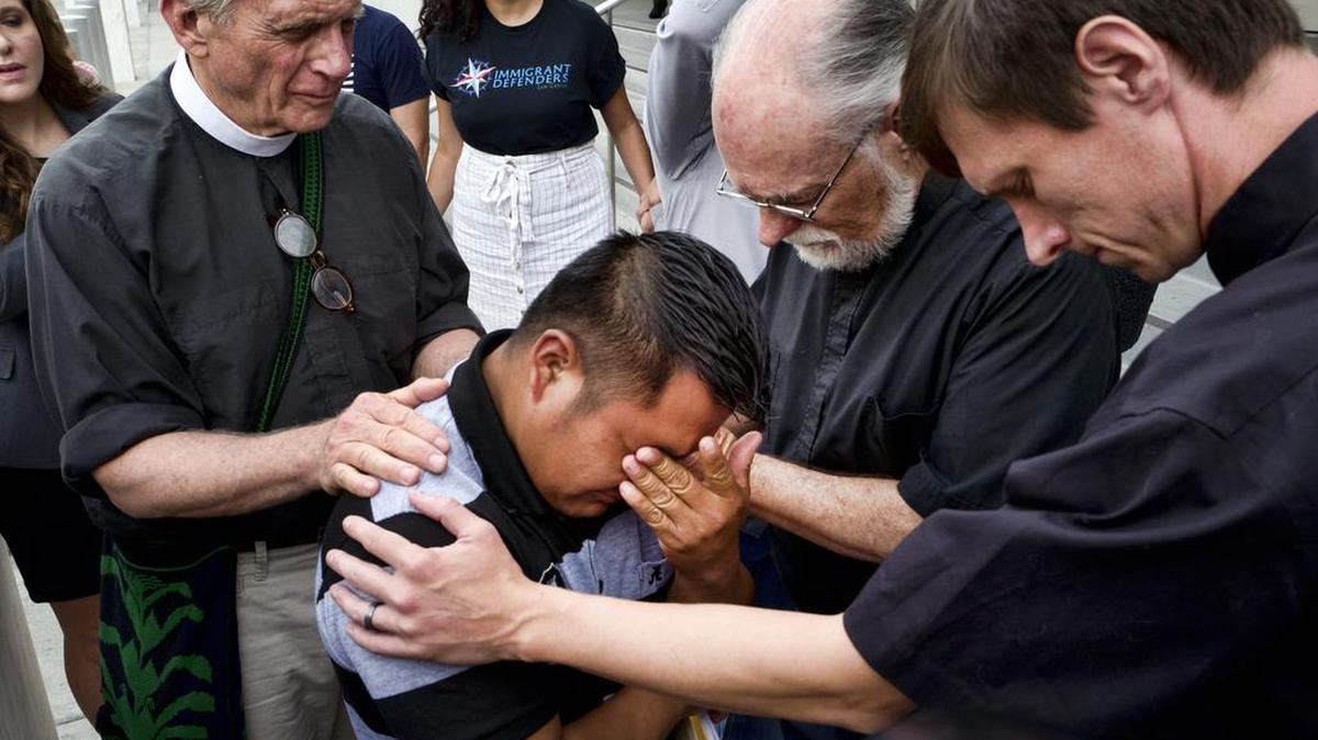 El padre Tom Carey (izq.) y los reverendos David Farley y Matthias Peterson-Brandt (der.) rezan junto al inmigrante guatemalteco Hermelindo Che Coc antes de una audiencia de inmigración en Los Angeles, el 10 de julio. Che Coc dijo que lo separaron en la frontera de su hijo de seis años, a quien enviaron a un albergue en Nueva York.