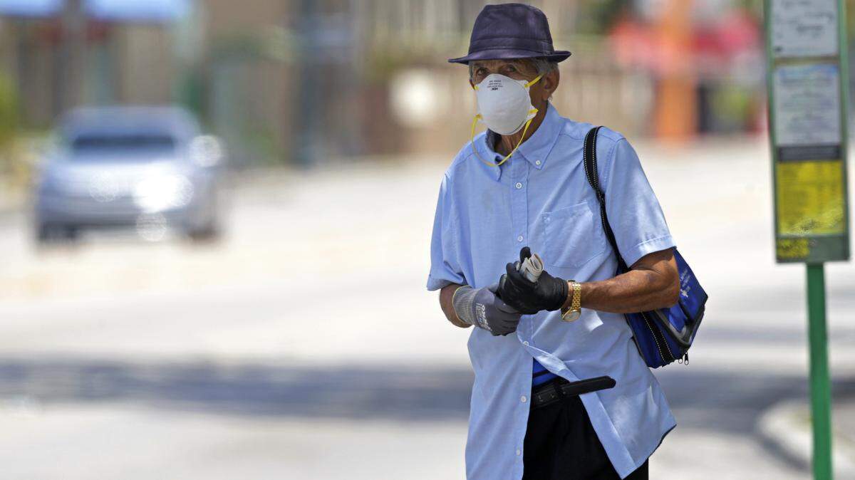 A man wearing a protective mask and gloves waiting at the bus stop located at SW 8 St & SW 55 Ave in Miami as the coronavirus pandemic continues on Monday, April 6, 2020.