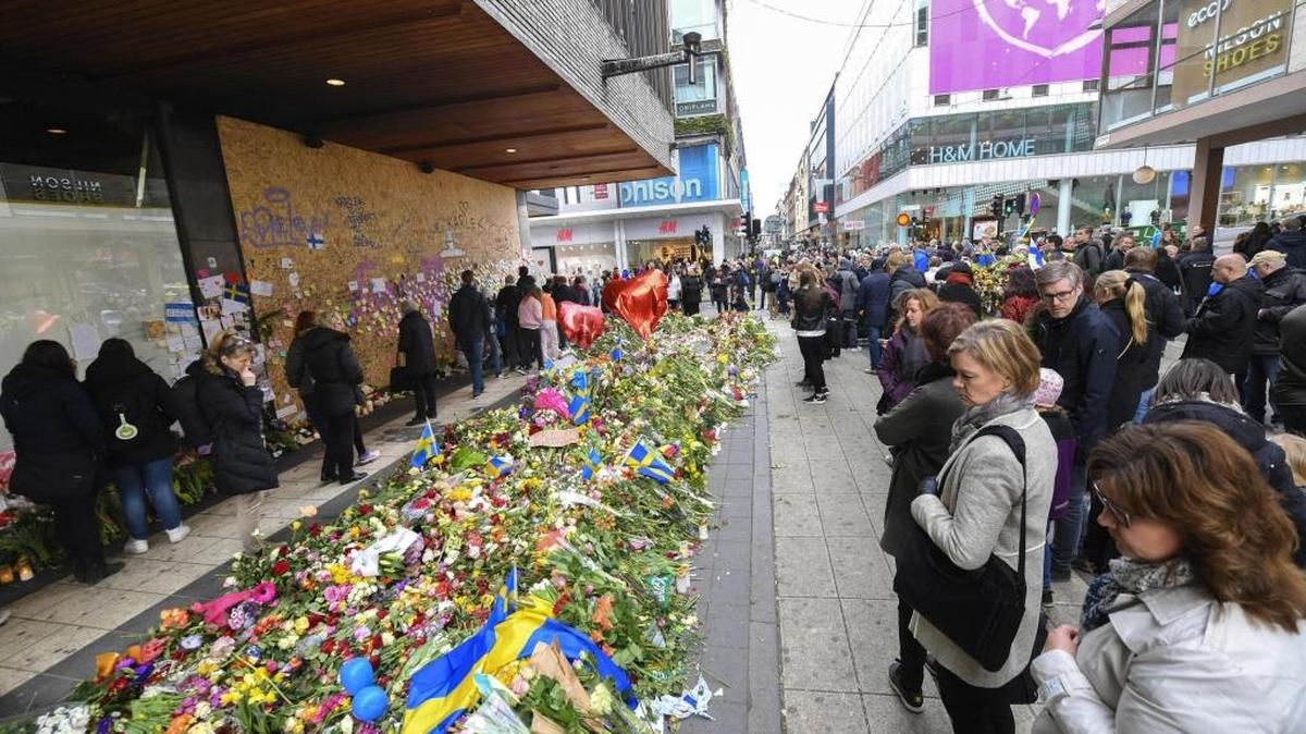 Varias personas caminan entre las flores colocadas en un memorial improvisado en la calle peatonal de Drottninggatan, donde tuvo lugar el ataque terrorista el 7 de abril, en Estocolmo, Suecia.