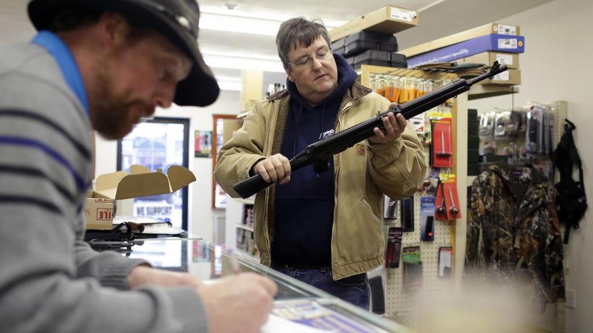 Un cliente inspecciona un fusil Saiga AK-47 mientras el dueño de la armería Big Rich American Sports, en Scranton, Pensilvania, verifica sus antecedentes antes de venderle el arma.