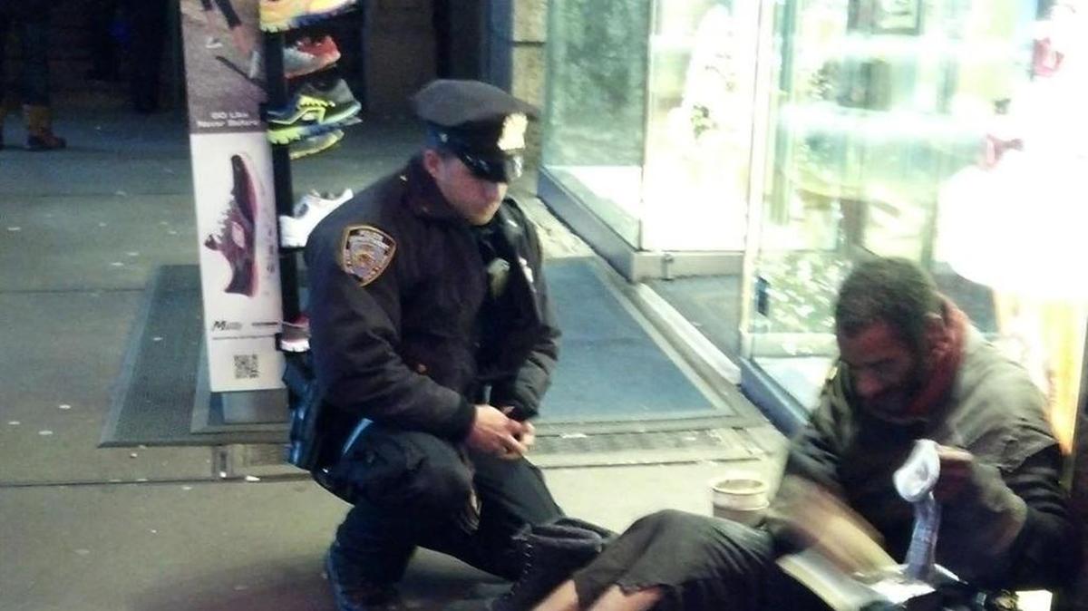 This photo provided by Jennifer Foster shows New York City Police Officer Larry DePrimo presenting a barefoot homeless man in New York’s Time Square with boots Nov. 14, 2012 . Foster was visiting New York with her boyfriend on Nov. 14, when she came across the shoeless man asking for change in Times Square. As she was about to approach him, she said the officer came up to the man with a pair of all-weather boots and thermal socks on the frigid night. She took the picture on her cellphone. It was posted Tuesday night to the NYPD’s official Facebook page and became an instant hit. More than 350,000 users “liked” it as of Thursday afternoon, and over 100,000 shared it. (AP Photo/Jennifer Foster)