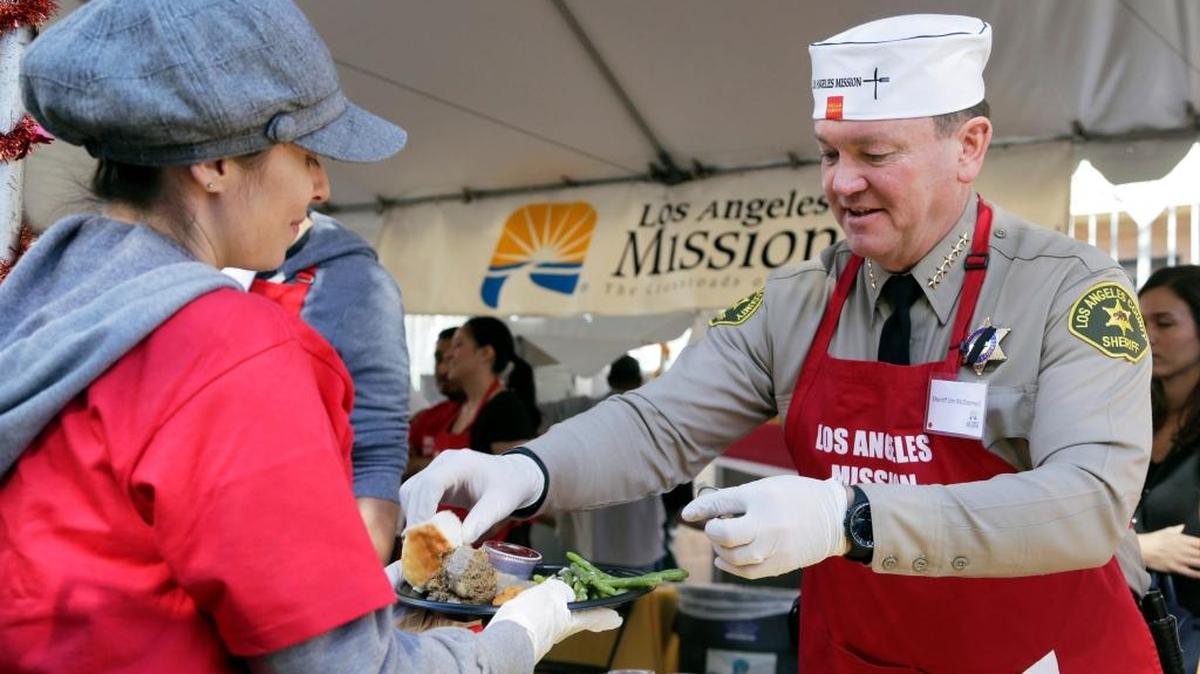 El sheriff del condado de Los Angeles, Jim McDonnell, sirve a una voluntaria en un evento para desamparados.
