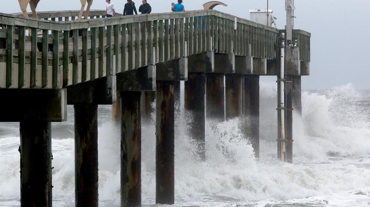 Varias personas observan el oleaje que bate un muelle en San Agustín, mientras el huracán Matthew avanza a lo largo de la costa de la Florida.