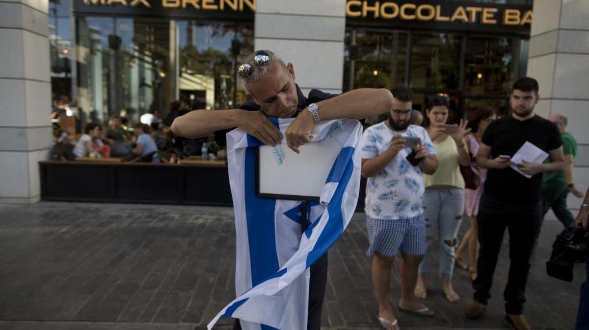 Un israelí pone una bandera frente al restaurante Max Brenner en el mercado Sarona, el 9 de junio, en Tel Aviv. Cuatro personas murieron en un atentado terrorista.