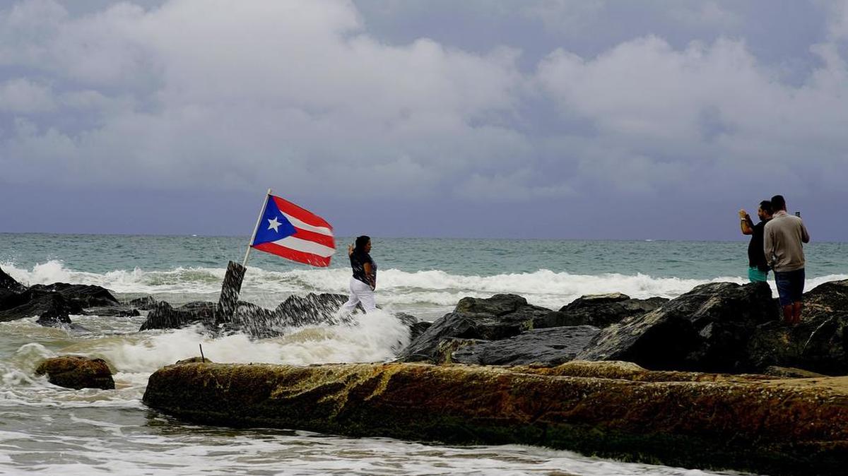 Una mujer posa para tomarse una foto con la bandera de Puerto Rico en la costa de San Juan, el miércoles, un día después que la tormenta tropical Dorian pasó cerca de la isla.