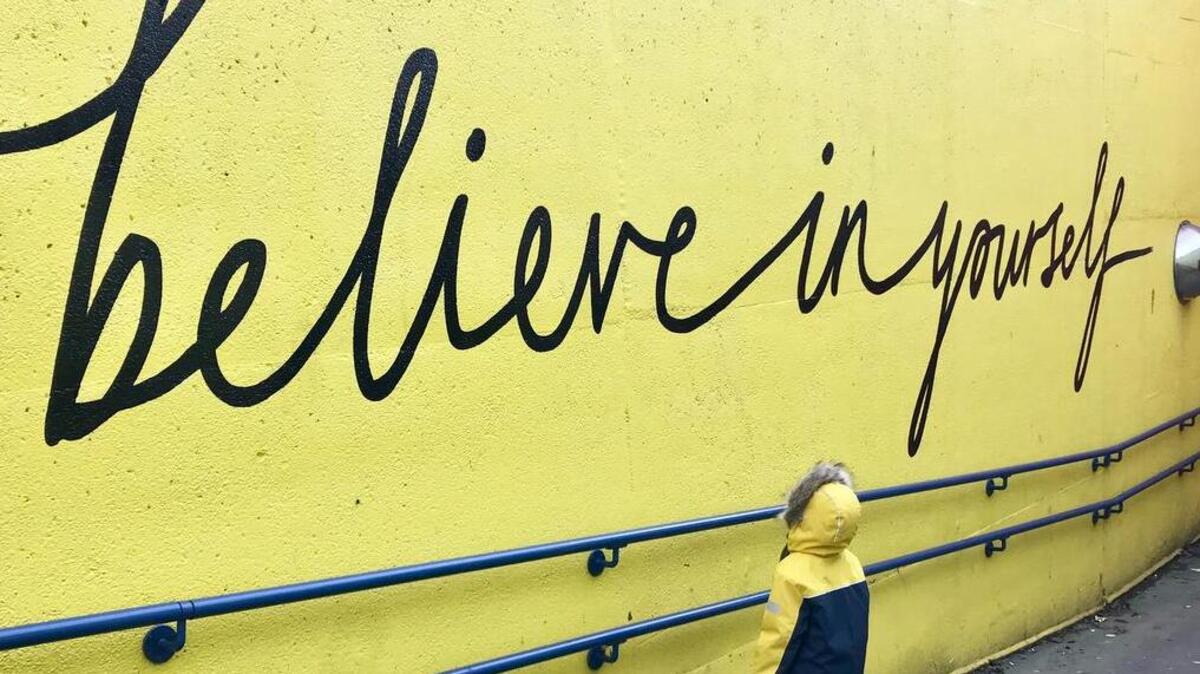 Un niño lee un graffiti que dice “cree en ti”.