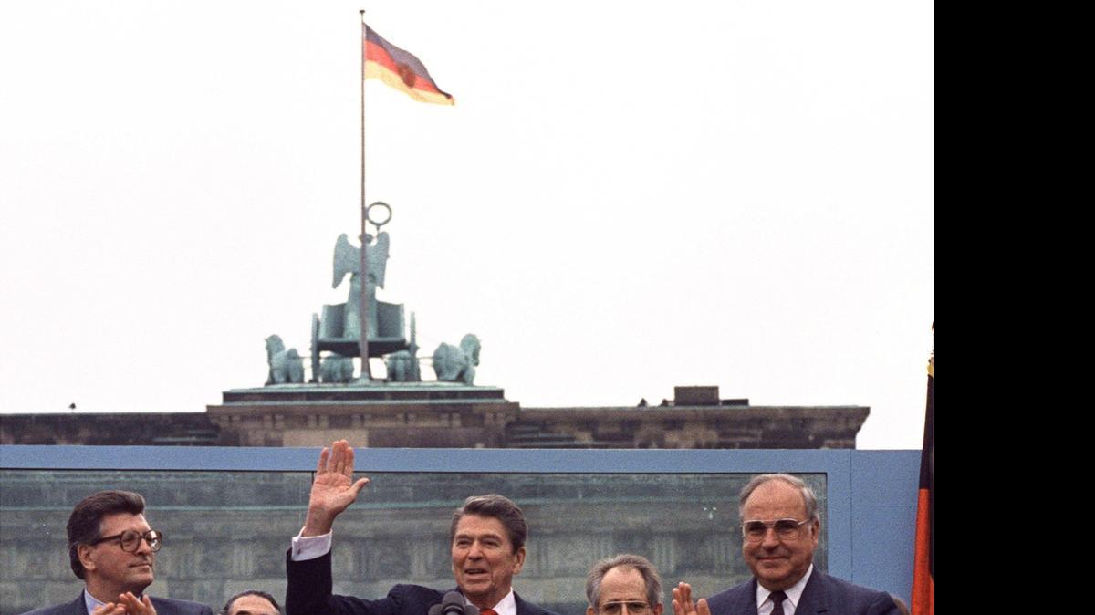 
El Presidente Ronald Reagan (centro) frente a la Puerta de Brandenburgo, en Berlín Oeste el 12 de junio de 1987, pronunció la famosa frase que terminaría con la caída del Muro de Berlín: ‘Mr. Gorbachev, tumbe este muro”. A su lado aplauden, el canciller alemán, Helmut Kohl (der.), y el presidente del Parlamento, Philipp Jenninger.


