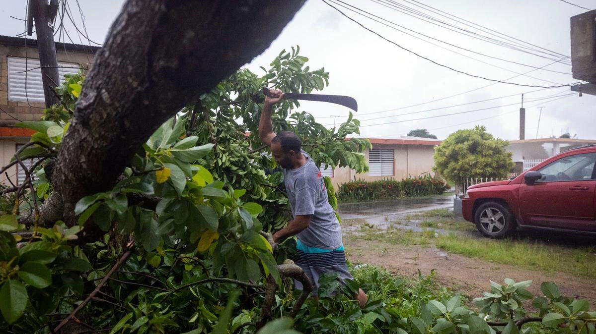 Un hombre usa un machete para cortar un árbol derribado por los vientos del huracán Fiona, en Loiza, Puerto Rico, el lunes 19 de septiembre de 2022. (AP foto/Alejandro Granadillo)
