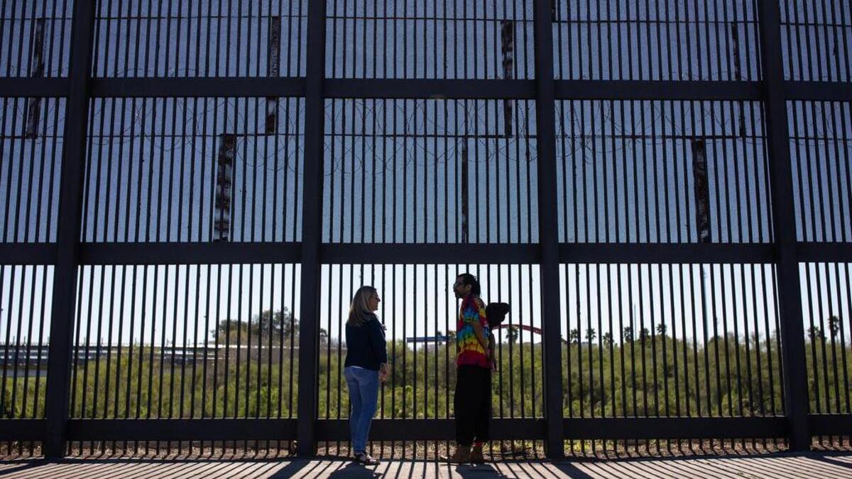 Jennifer Clark y Jey Sushil miran en dirección a Matamoros, México, a través de una parte de la cerca en la frontera entre Estados Unidos y México en Brownsville, Texas.