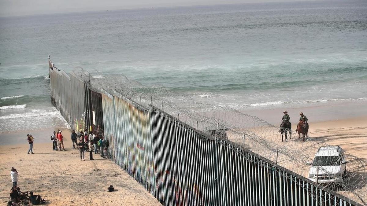 Un grupo de personas mira a través de la reja a agentes de la patrulla fronteriza de EEUU, en la división que separa a México de Estados Unidos en el océano Pacífico, en Tijuana, el lunes.