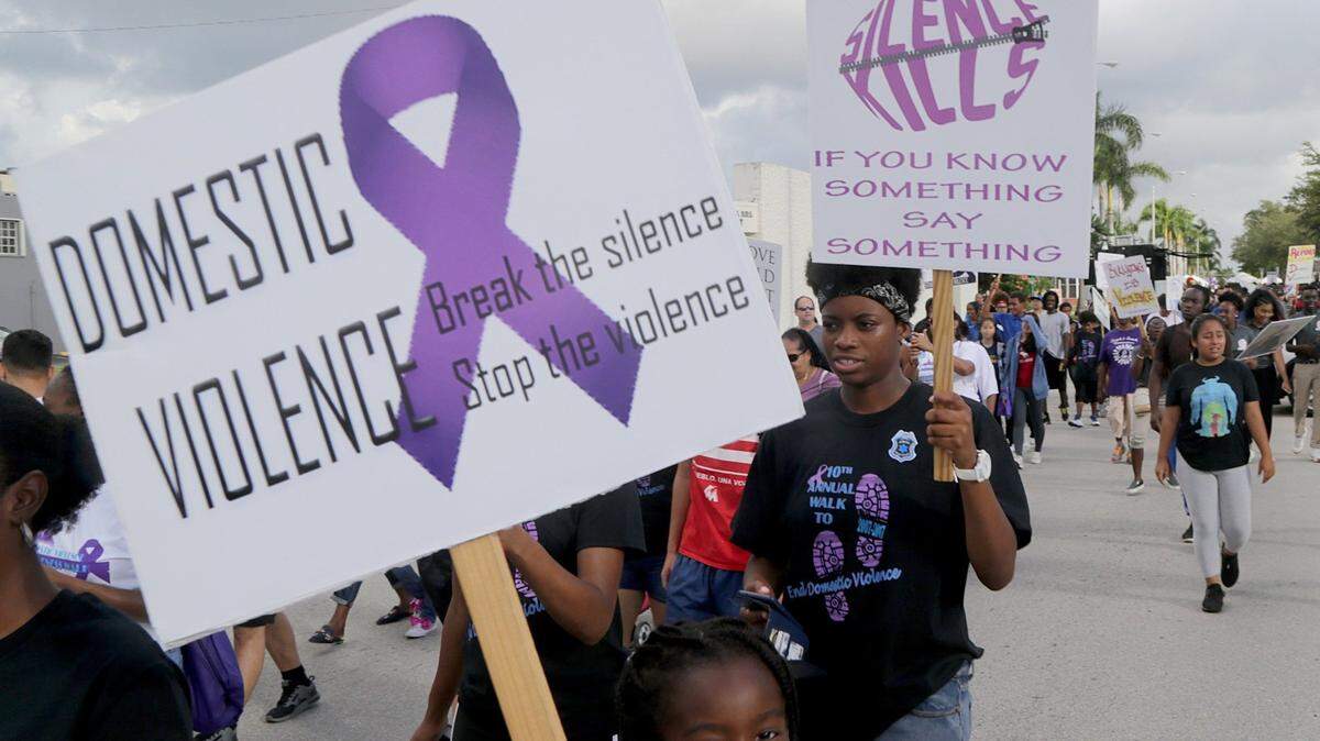 Mujeres, hombres y jóvenes participan en una marcha en contra de la violencia doméstica, el 6 de octubre de 2018 en North Miami Beach, Florida. Las pancartas dicen “Violencia doméstica: Rompe el silencio y detén la violencia”, y “El silencio mata, si sabes algo, di algo”.