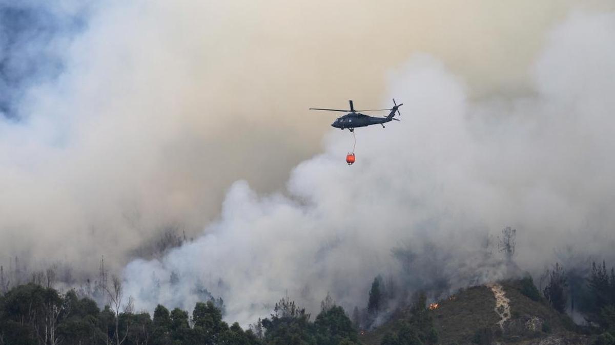Un helicóptero rocía agua sobre un fuego forestal en las montañas que rodean a Bogotá.