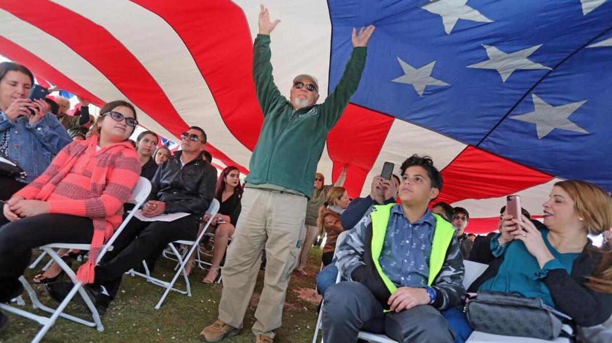Voluntarios del Servicio Nacional de Parques levantan una bandera estadounidense sobre ciudadanos recién naturalizados en el Parque Nacional de Biscayne National, donde el USCIS realizó una ceremonia especial para 83 niños de 83 países, en enero del 2018.