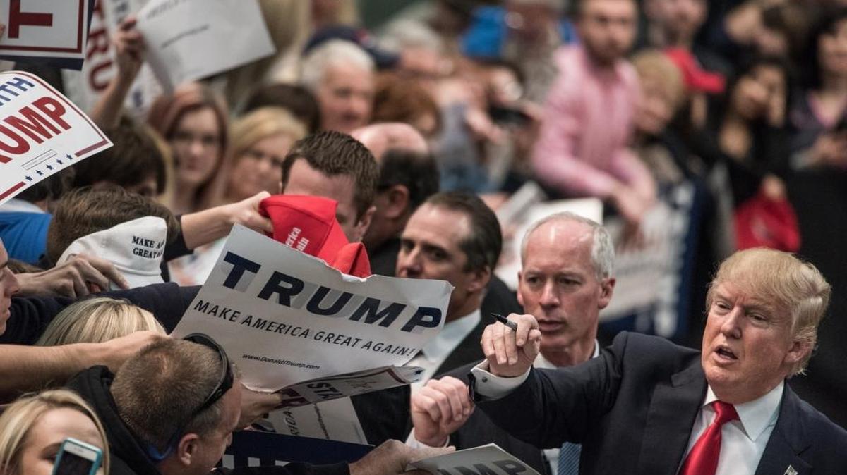 El candidato republicano Donald Trump (der.) firma autógrafos en un acto de la campaña en Concord, Carolina del Norte, el lunes.