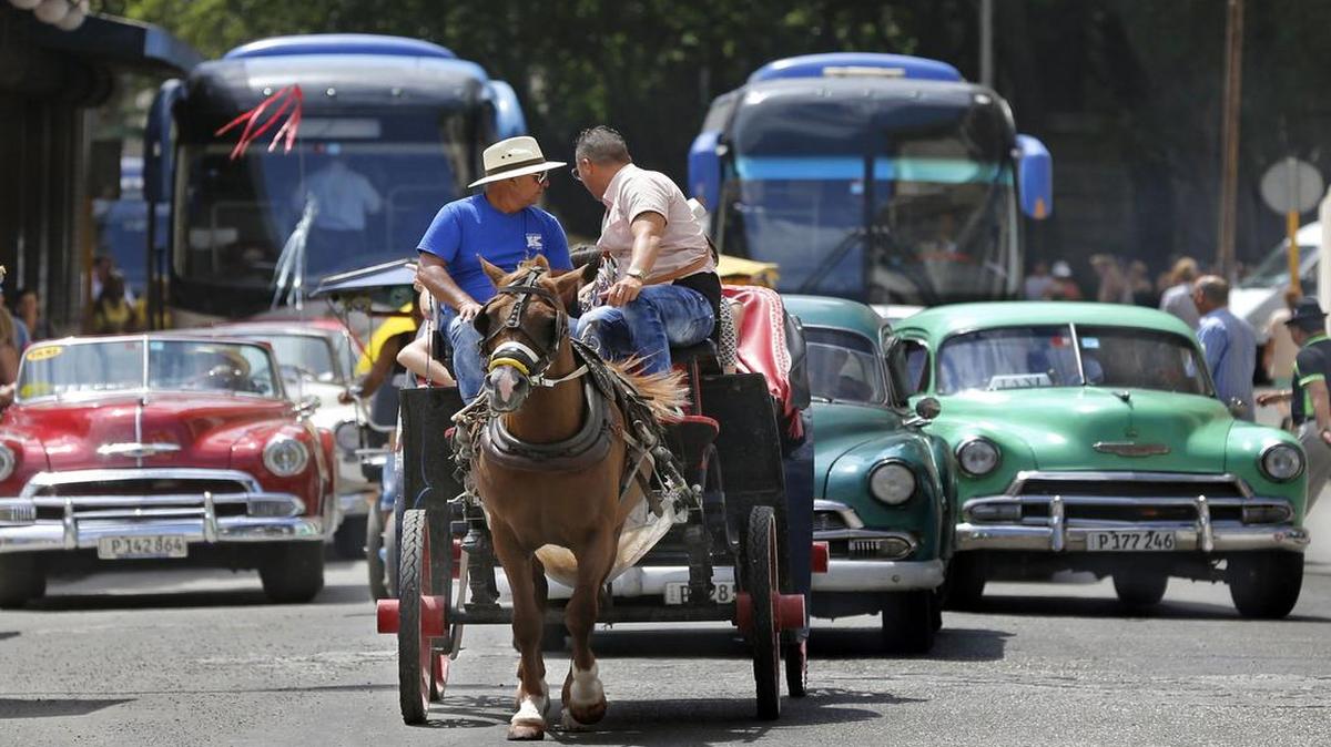 Autobuses turísticos comparten una calle de La Habana con autos antiguos y un coche tirado por un caballo.