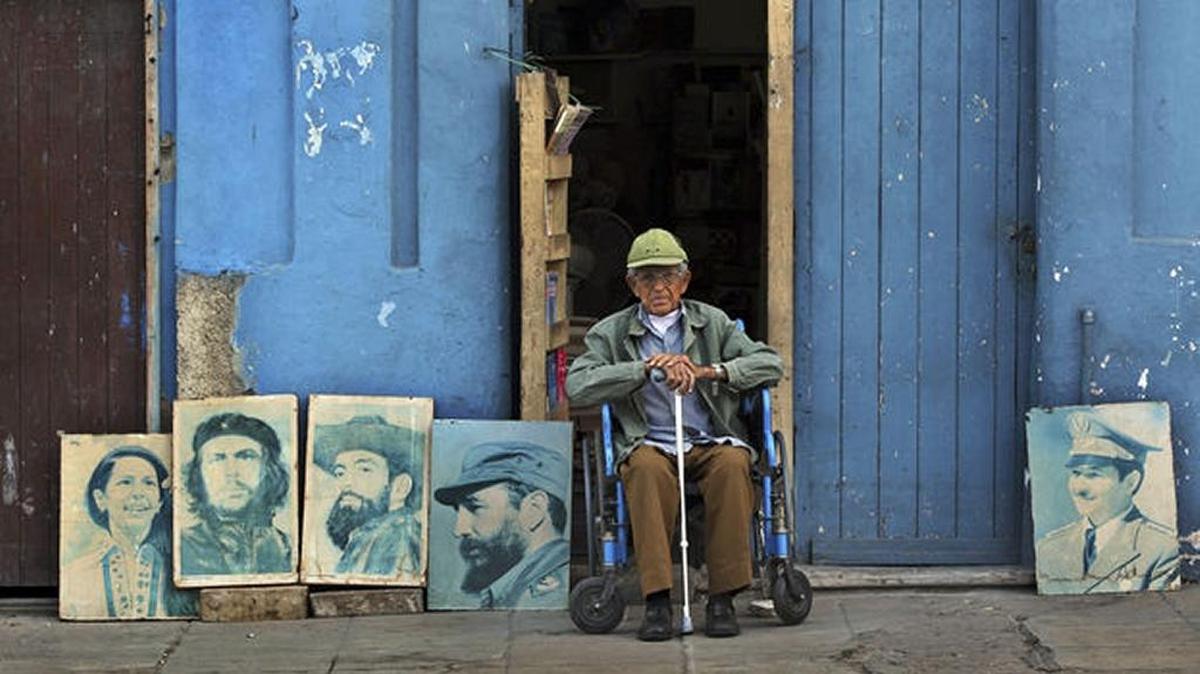 Un anciano posa junto a una serie de retratos de líderes cubanos.