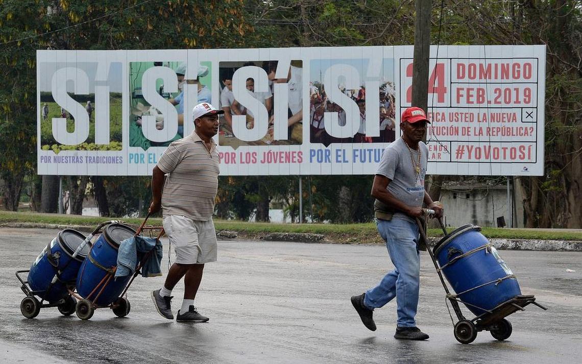 Two men walk near a government campaign billboard in Havana that encourages Cubans to vote for the new constitution. A referendum on the constitution is being held Sunday.
