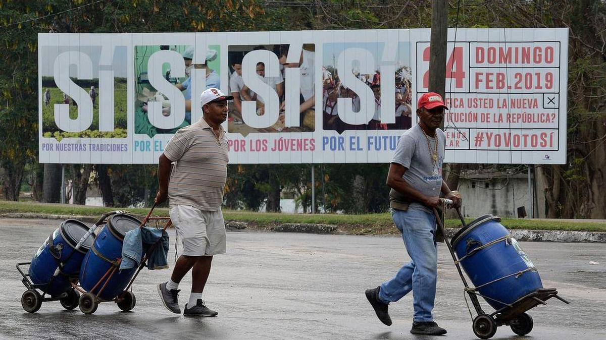 Dos hombres caminan frente a un anuncio que promueve la participación en el referendo constituyente, el 13 de febrero en La Habana.