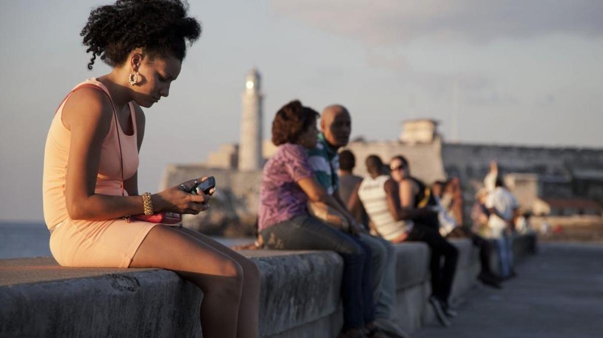 Una mujer observa el teléfono celular en el Malecón habanero.