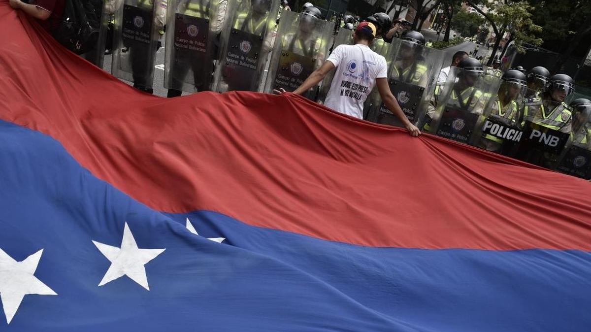 Manifestantes llevan una bandera venezolana frente a fuerzas de la Policía Nacional en una protesta en apoyo al referendo revocatorio, en Caracas, el 18 de mayo.