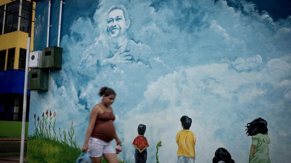 Una mujer camina frente a un mural con la imagen de Hugo Chávez, en Sabaneta, Venezuela.